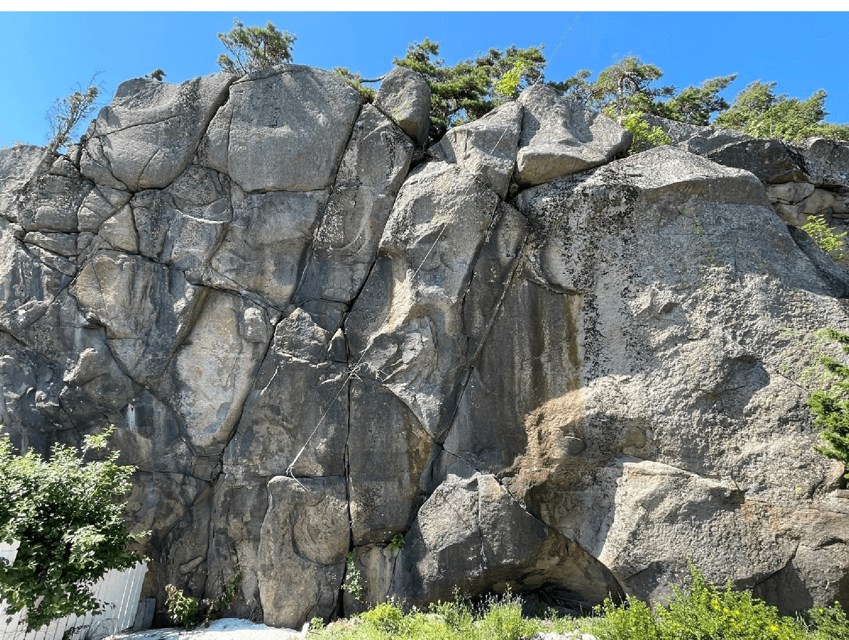 Høy, oppsprukket bergskrent med store steinblokker og vegetasjon på toppen, langs Kyststien ved Faratangen.
