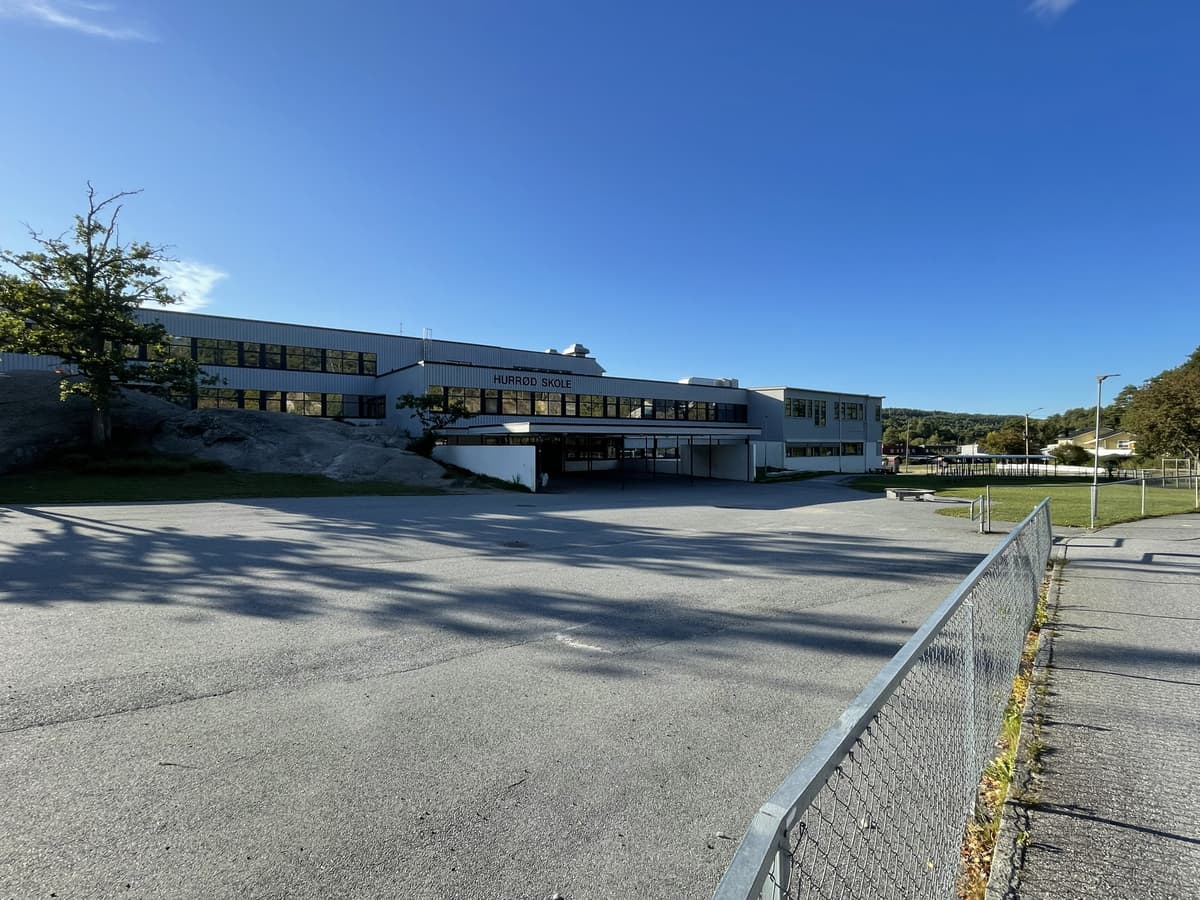Hurrød skole, en lang hvit toetasjes skolebygning, sett fra den tomme asfalterte skolegården.