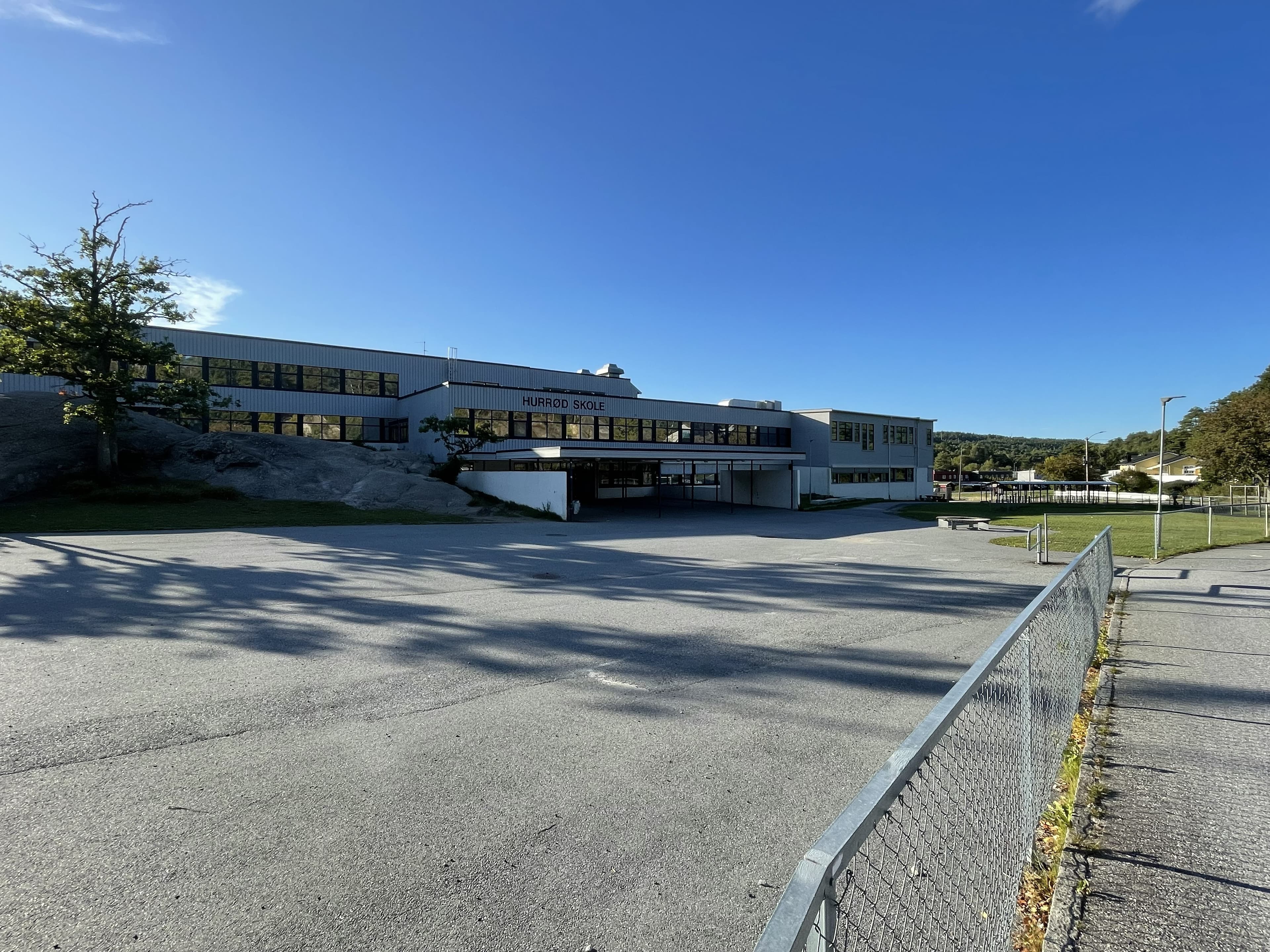 Hurrød skole, en lang hvit toetasjes skolebygning, sett fra den tomme asfalterte skolegården.